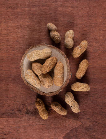 Top view raw peanuts on wooden stand on brown background