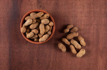 Top view raw peanuts in bowl on wooden brown background horizontal