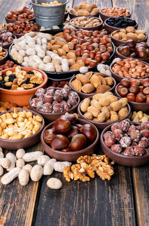 Assorted nuts and dried fruits in a different bowls and plates with pecan, pistachios, almond, peanut, cashew, pine nuts high angle view on a woodenの写真素材