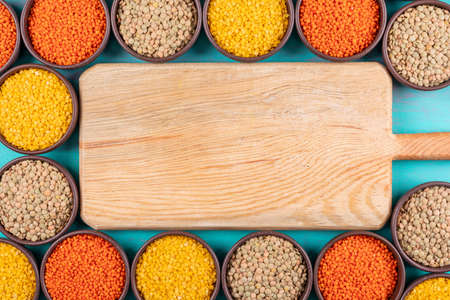 Red and yellow lentils in a bowls with wooden cutting board flat lay on a light blue background copy...