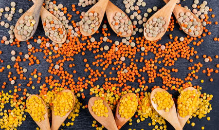 High angle view yellow and green lentils in wooden spoons on black stone background. horizontal free...