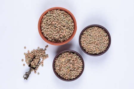 Top view green lentils in brown bowls and iron spice spoon on white background. horizontalの写真素材