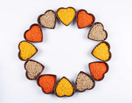 Yellow, green and red lentils in a heart shaped bowls top view on a white background free space for...