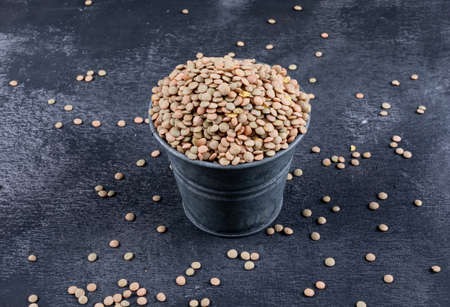 High angle view green lentils in black mini bucket on black stone background. horizontal