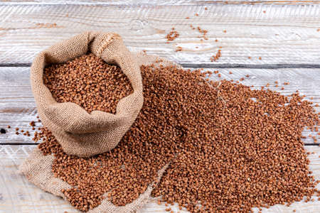 Buckwheats in a sack and around on a light wooden background. top view.