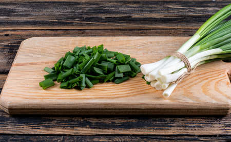 High angle view spring onions or scallions on cutting board with chopped up spring onions on dark wooden background. horizontalの写真素材