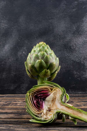 Side view artichoke and a slice on dark wooden and black background. horizontal space for text