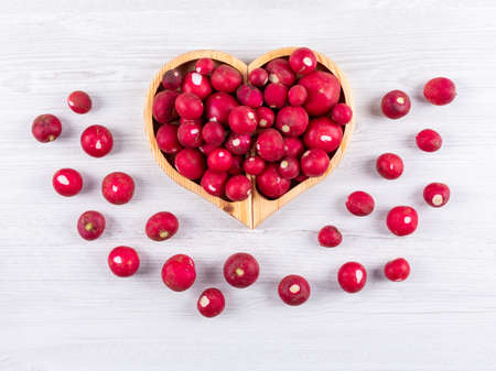 Top view red radishes in heart shaped plate on white wooden texture background. horizontalの写真素材