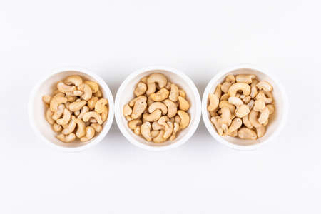 Some of cashew in a three white bowl on white background, top view. free space for your text