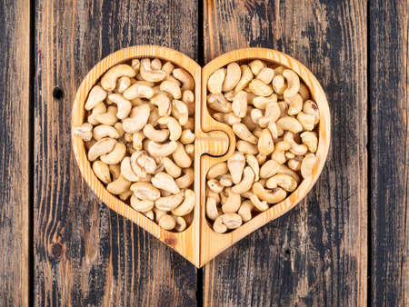 Cashew in a heart shaped wooden plate top view on a wooden backgroundの写真素材