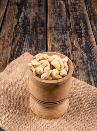 Cashew in a wooden cup side view on a piece of sack and wooden textured backgroundの写真素材
