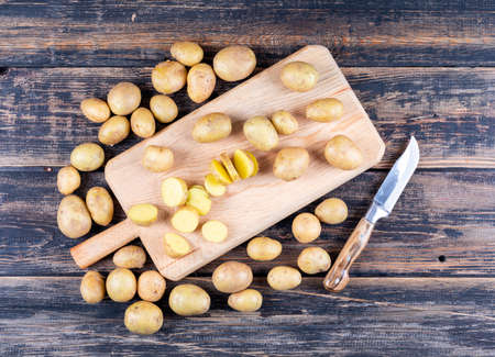Set of knife and chopped up potatoes on a cutting board on dark wooden background. top view.の写真素材