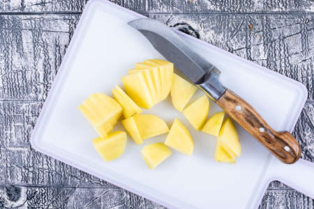 Chopped potatoes on a cutting board with knife top view on a gray wooden backgroundの写真素材