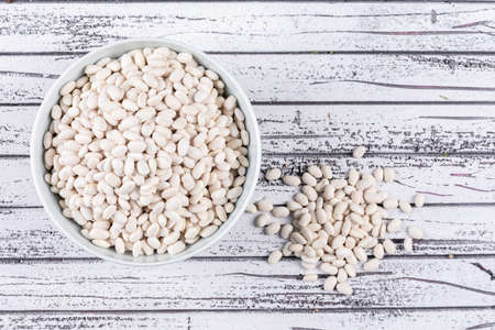 Some white beans in bowls and aside on gray wooden background, top view.