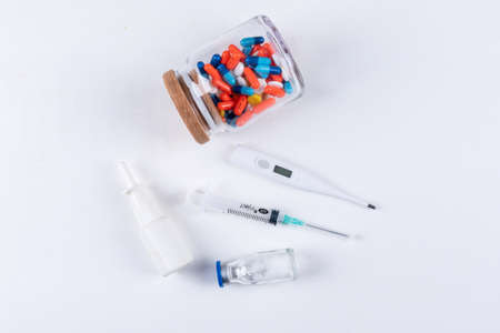 Set of thermometer, nasal spray, needle and pills in a jar on a white background. flat lay.