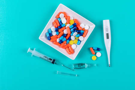 Top view pills in bowl with thermometer, needles on cyan blue background. horizontal
