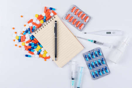 Top view colorful pills with notepad, pen, thermometer, nasal spray and needle on white background. horizontalの写真素材