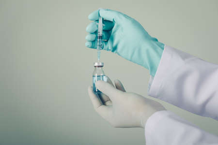 Side view doctor with gloves drawing medicine out of a vial on gray background. horizontalの写真素材
