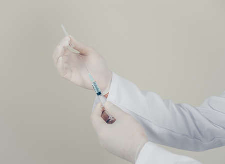 Side view doctor with gloves uncapping the syringe on gray background. horizontal