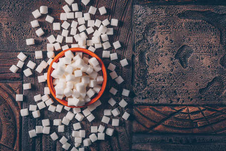 Flat lay white sugar cubes in orange bowl on dark wooden background. horizontal space for text