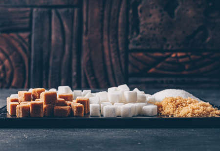 Brown and white sugar in a cutting board on a dark background. side view. free space for your text