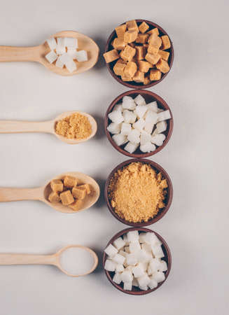 Top view white and brown sugar in bowls with spoons on white background. vertical
