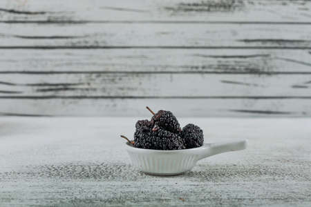 Side view mulberries in small bowl on light wooden background. horizontal free space for your textの写真素材