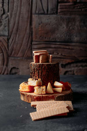 Side view waffles on wood slice with fruits and cakes on black textured and wooden background....