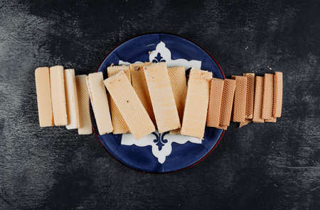Some waffles in a plate on black textured background, top view.