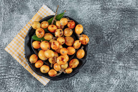 Loquats in a bowl on a cloth and gray textured background. top view. space for textの写真素材