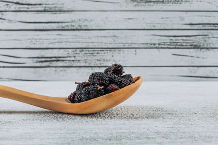 Mulberries in a wooden spoon side view on a light wooden background free space for your textの写真素材