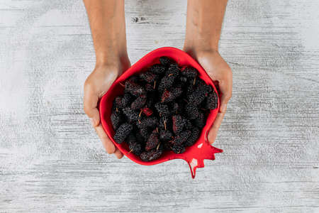 Man holding mulberries in a pomegranate shaped bowl on a light wooden background. top view.の写真素材