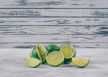 Side view green lemons with slices on gray wooden background. horizontal