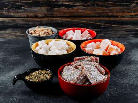 Some turkish delight lokums with pistachio in a bowls on black textured background, side view.