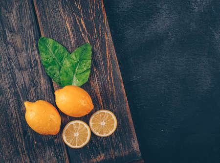 Top view lemons with leaves and slices on wooden tray and black textured background. horizontal space for textの写真素材