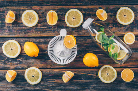 Lemons with fruit juicer and glass bottle flat lay on a dark wooden backgroundの写真素材