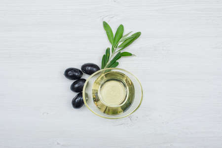 Black olives and olive oil in a glass can with olive leaves top view on a white wood plank backgroundの写真素材