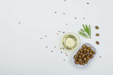 Green olives with a jar of olive oil, spices and olive leaves in a white plate on white background, top view.の写真素材