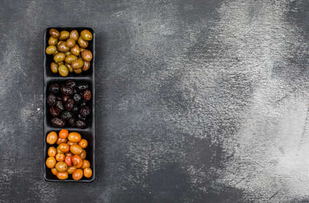 Fresh marinated olives in a black plate on a dark grey grunge background. top view.