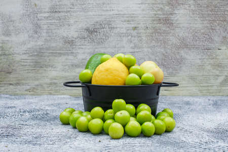 Greengages, pears and lemon in a black saucepan on a grungy blue and grey wooden background. side...