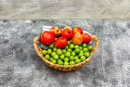 Peaches and greengages in a wicker basket and picnic cloth on grunge grey and wooden background, high angle view.の写真素材