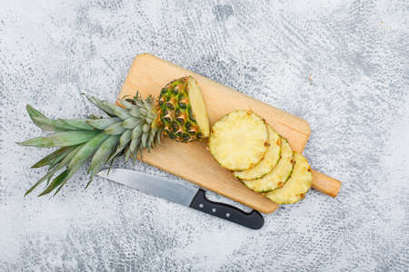 Sliced cool pineapple with a knife in a chopping board on grunge background, flat lay.の写真素材