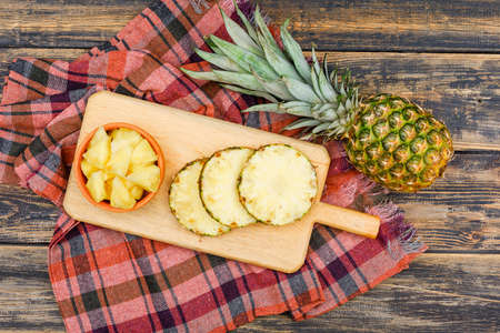 Whole and sliced pineapple in a cutting board and clay bowl on a wooden grunge and picnic cloth background. flat lay.の写真素材