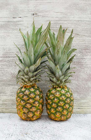 Two aromatic pineapples on grey wall and grungy background, side view.