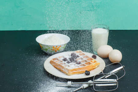 High angle view waffles in plate with eggs, flour, milk, mixer sticks on dark and cyan background. horizontal の写真素材
