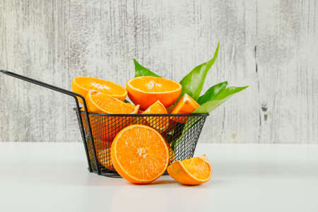Fleshy orange with leaves in a black colander on grunge and white background. side view. 