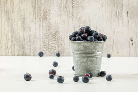 Tasty ripe blueberries in a small metal bucket on white and grunge background, side view.の写真素材