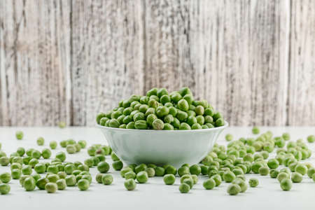 Peas in a white bowl on white and grungy wooden background. side view.