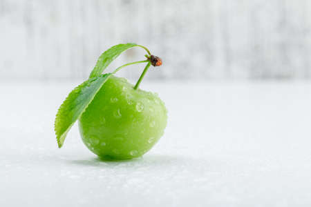 Green plum with leaves on grungy and white background, side view. 