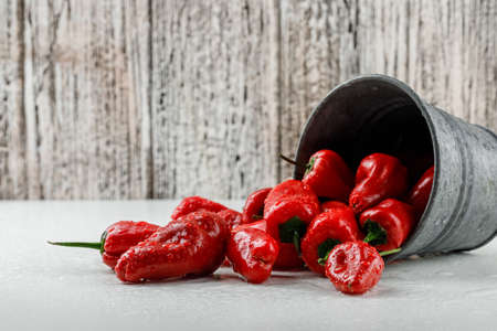 Scattered red peppers from a mini bucket on white and wooden grunge background, side view. の写真素材